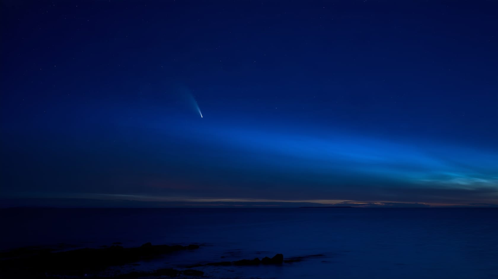 A comet low over a calm sea at night