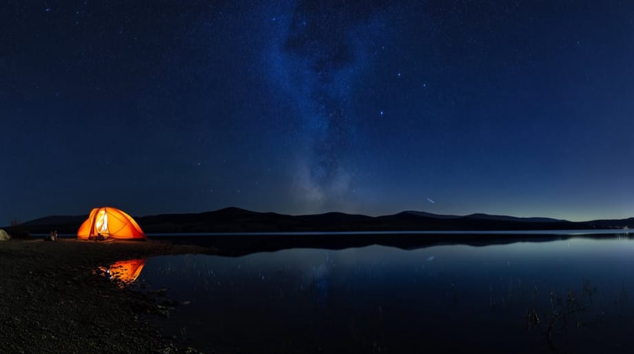 A lit tent on the shore of a mountain lake